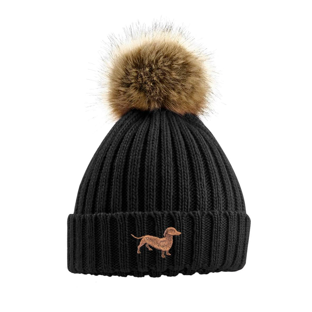 Black knit beanie with brown fur pom-pom and dachshund embroidery on a white background